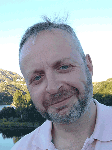 Man in pink shirt by a wooded lake
